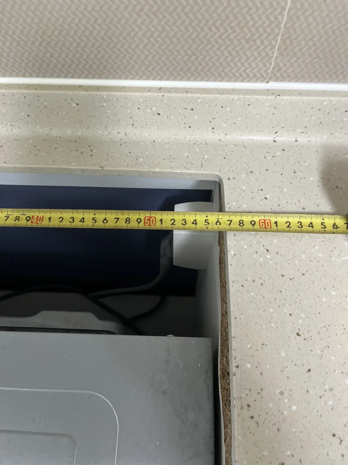 작업 전 인덕션을 들어낸 인조대리석 상판 개구부 안쪽의 금속 본체와 줄자로 치수를 재는 모습